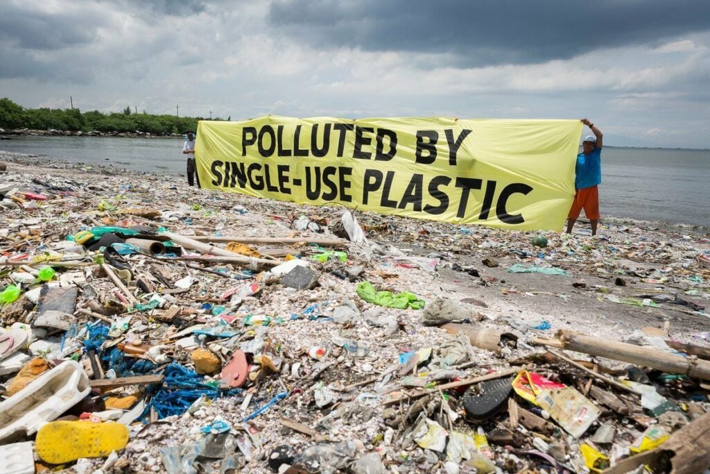 Heavily polluted beach covered in plastic waste with activists holding a banner reading 'Polluted by Single-Use Plastic,' emphasizing the environmental crisis caused by plastic pollution in oceans.